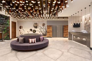 Un'area reception moderna con una zona salotto a forma di cerchio, una parete in legno con display digitale e una scrivania reception con TV a parete.