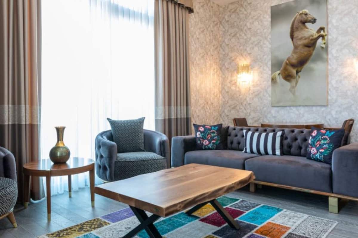 A modern living room with a grey sofa, a wooden coffee table, and a colorful rug. There is a vase on a side table and a painting of a horse on the wall.