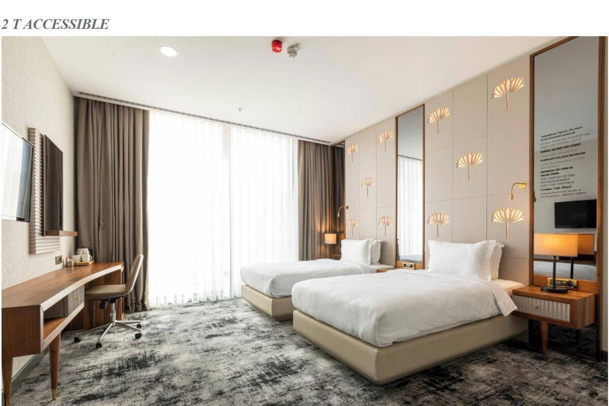 A hotel room with two beds, a desk, and a large window.