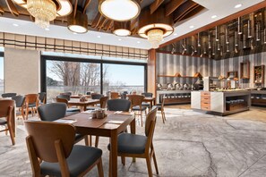 Un ristorante moderno con tavoli e sedie in legno, un'ampia vetrata e una cucina visibile attraverso lo spazio aperto.