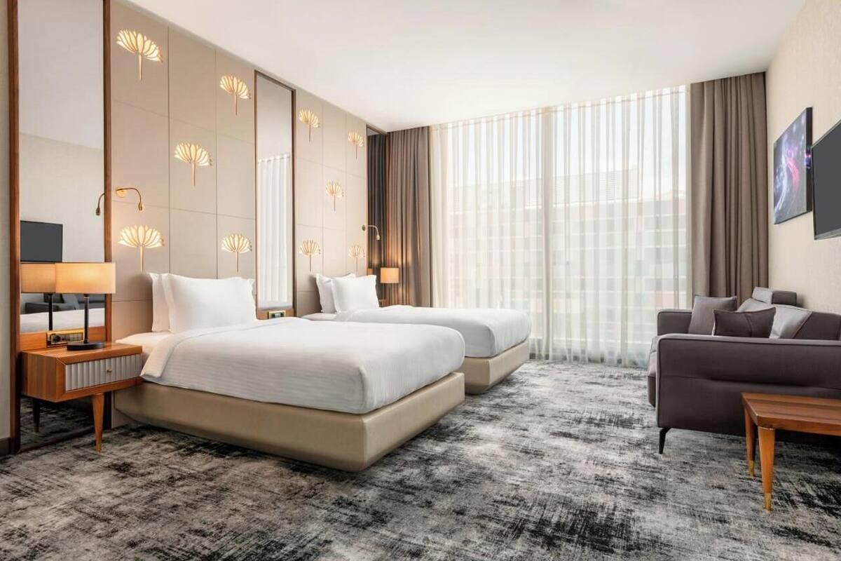 A hotel room with two beds, a sofa, a TV, and a large window with curtains.