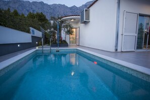 Une piscine avec une vue sur les montagnes, un bâtiment à l’extérieur blanc et une porte donnant sur un espace abrité.