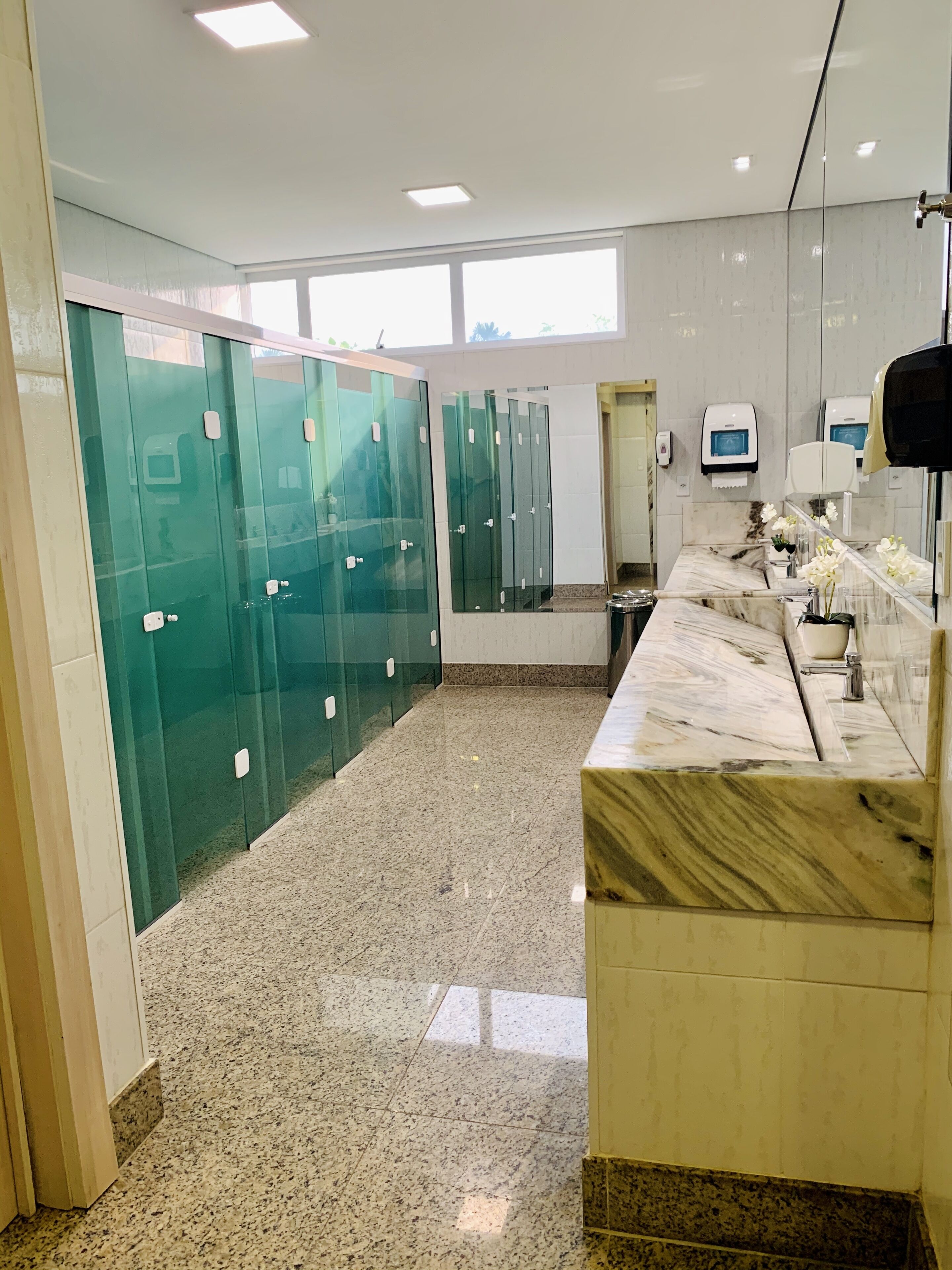A modern bathroom with glass lockers, marble countertops, and a large mirror.
