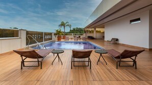Un área de piscina en la azotea con sillones de descanso, piscina y vista al cielo.