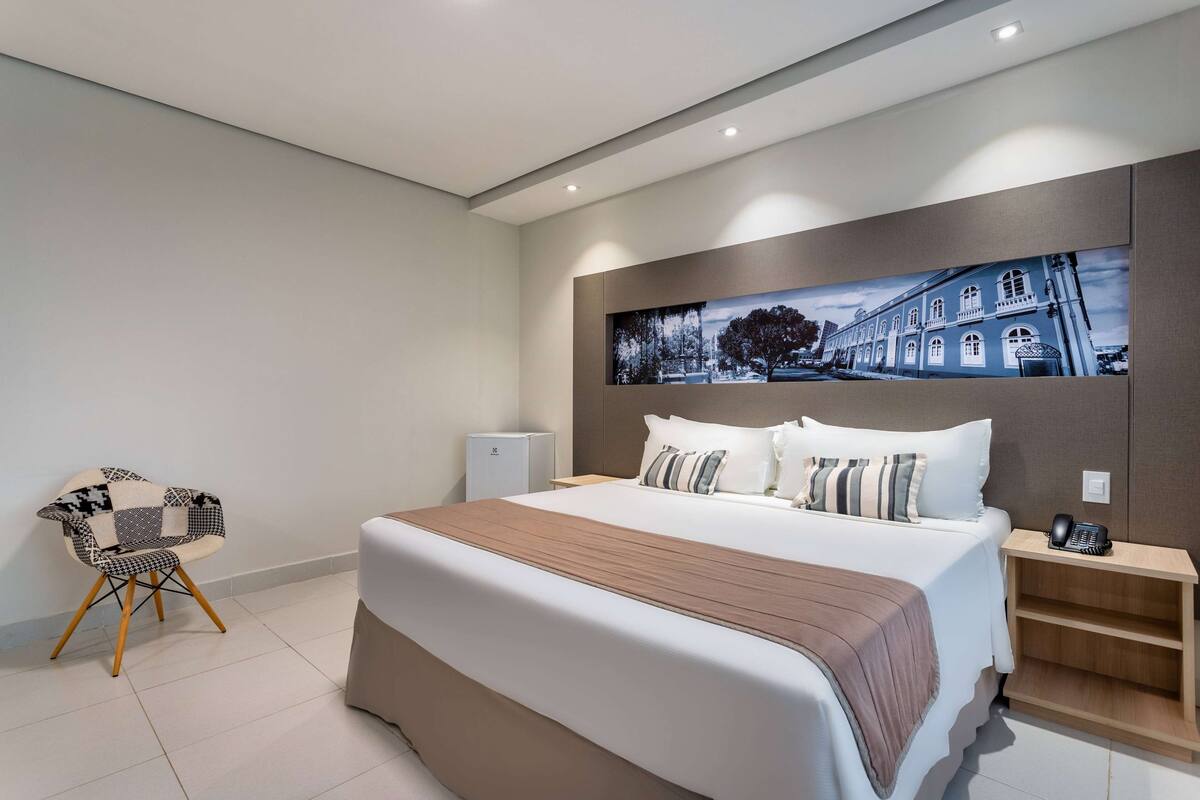 A modern hotel room with a large bed, a bedside table, a chair, and a wall-mounted phone.