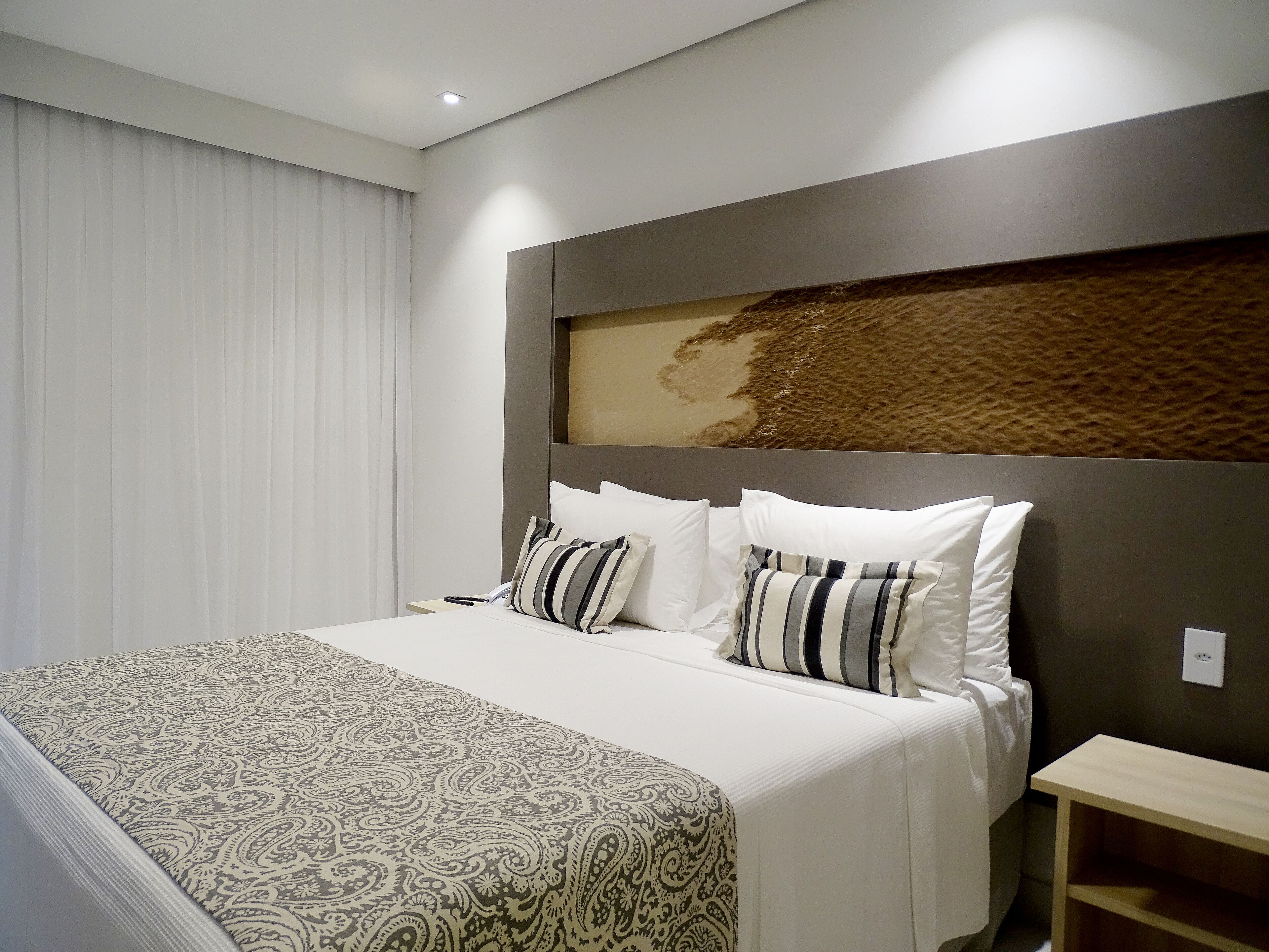 A hotel room with a large bed, a headboard with a textured design, and a bedside table.