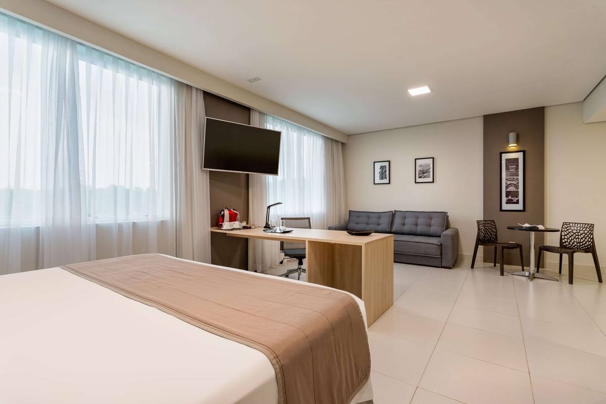A hotel room with a bed, a desk with a computer, a sofa, and a TV.