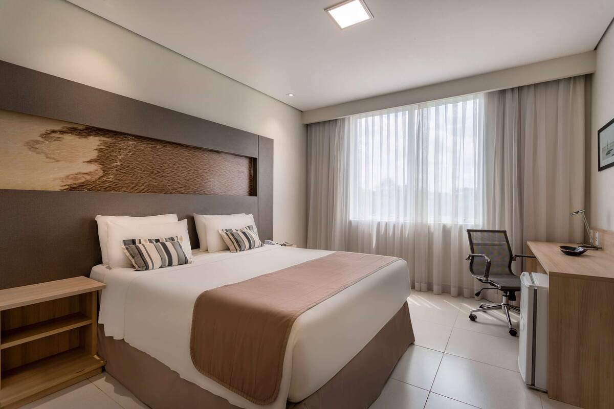 A modern hotel room with a large bed, a desk, and a chair.