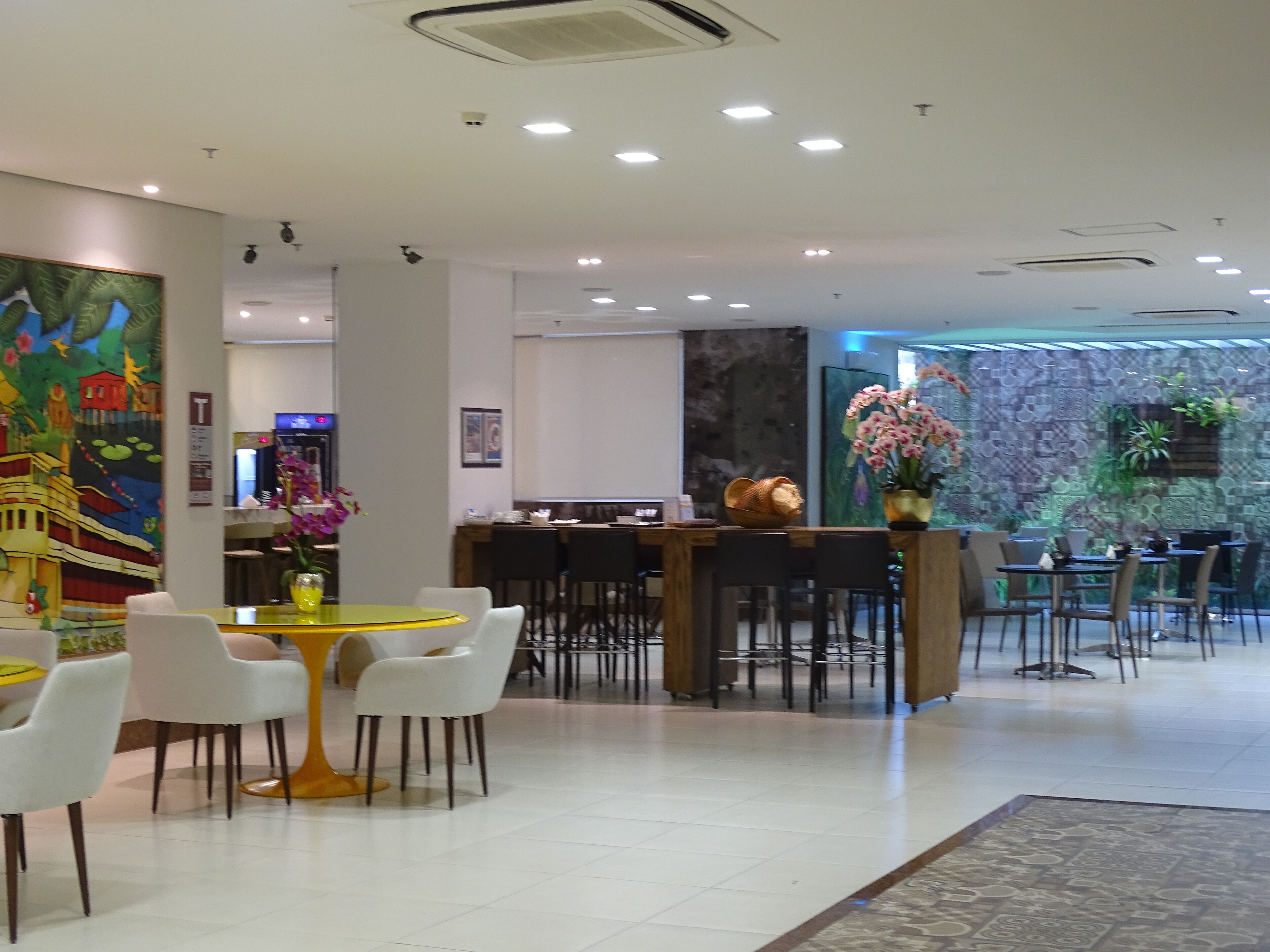 A modern hotel lobby with a reception desk, seating area, and decorative elements like a mural and potted plants.
