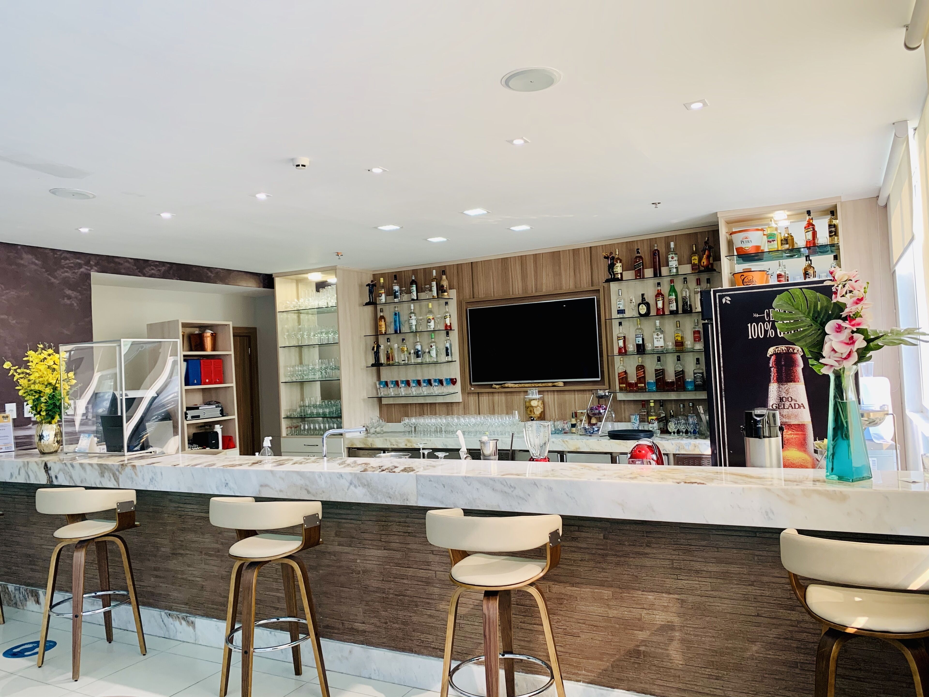 A modern bar area with a marble countertop, bar stools, a flat-screen TV, and a variety of liquor bottles.