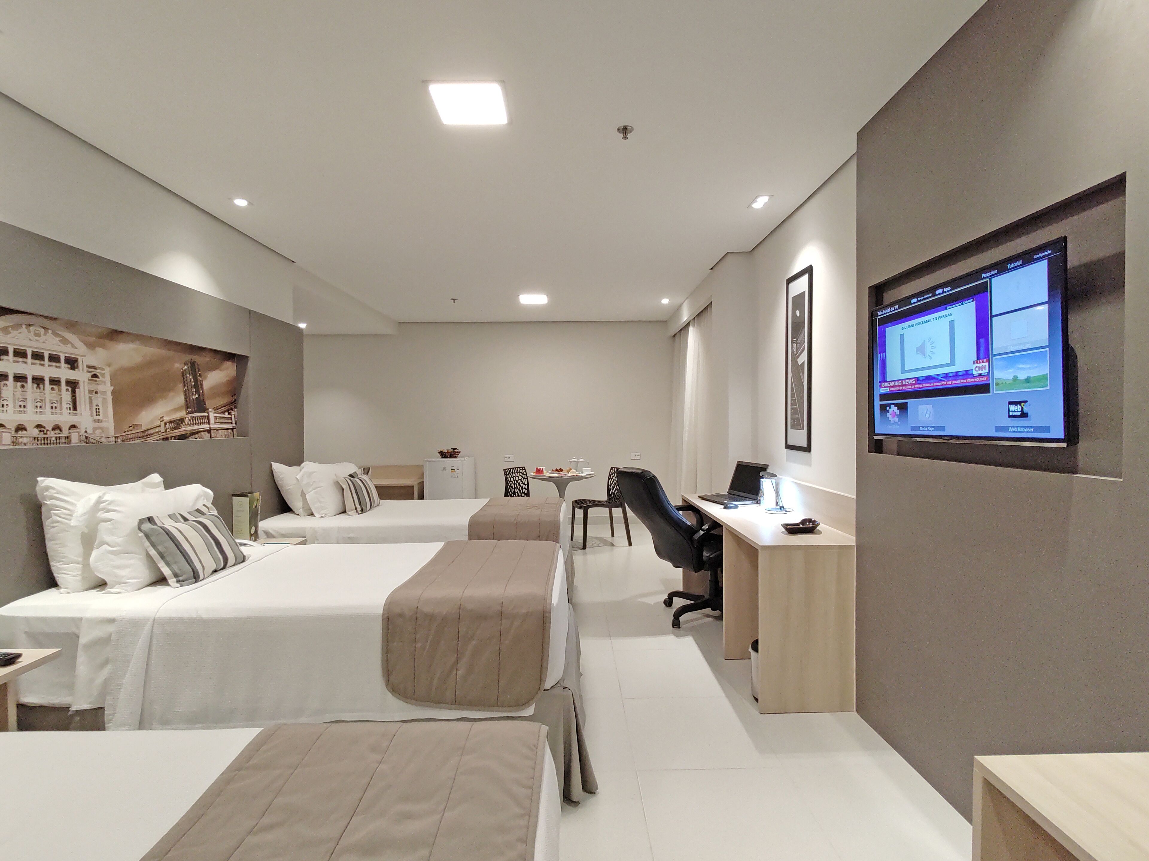 Une chambre d’hôtel avec deux lits, un bureau avec un ordinateur et un téléviseur fixé au mur.