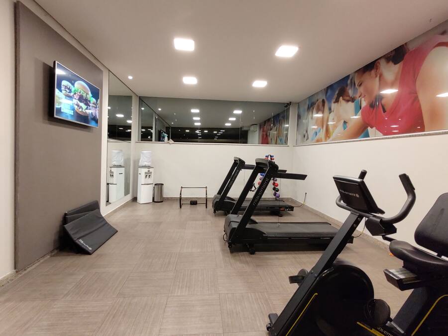 Un gimnasio con cintas de correr, una elíptica y una bicicleta estática. Hay dispensadores de agua y un espejo en la pared.