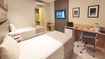 Una habitación de hotel con dos camas, un escritorio con computadora, una silla y un televisor en la pared.