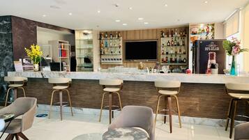 Een moderne bar met een marmeren aanrecht, barstoelen en diverse drankflessen.