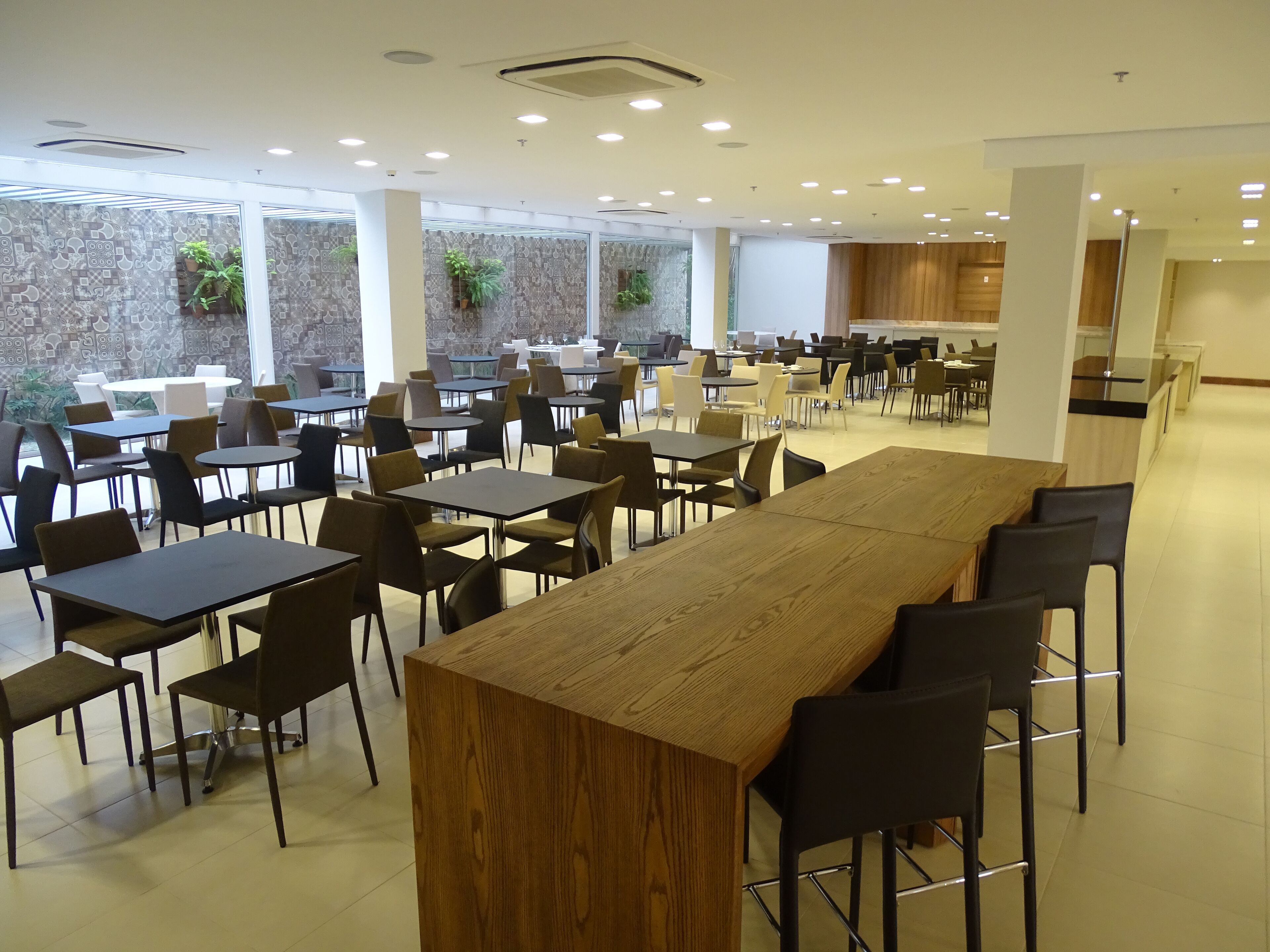 Eine großzügige Cafeteria mit mehreren Tischen und Stühlen, großen Fenstern und einem modernen Ambiente.