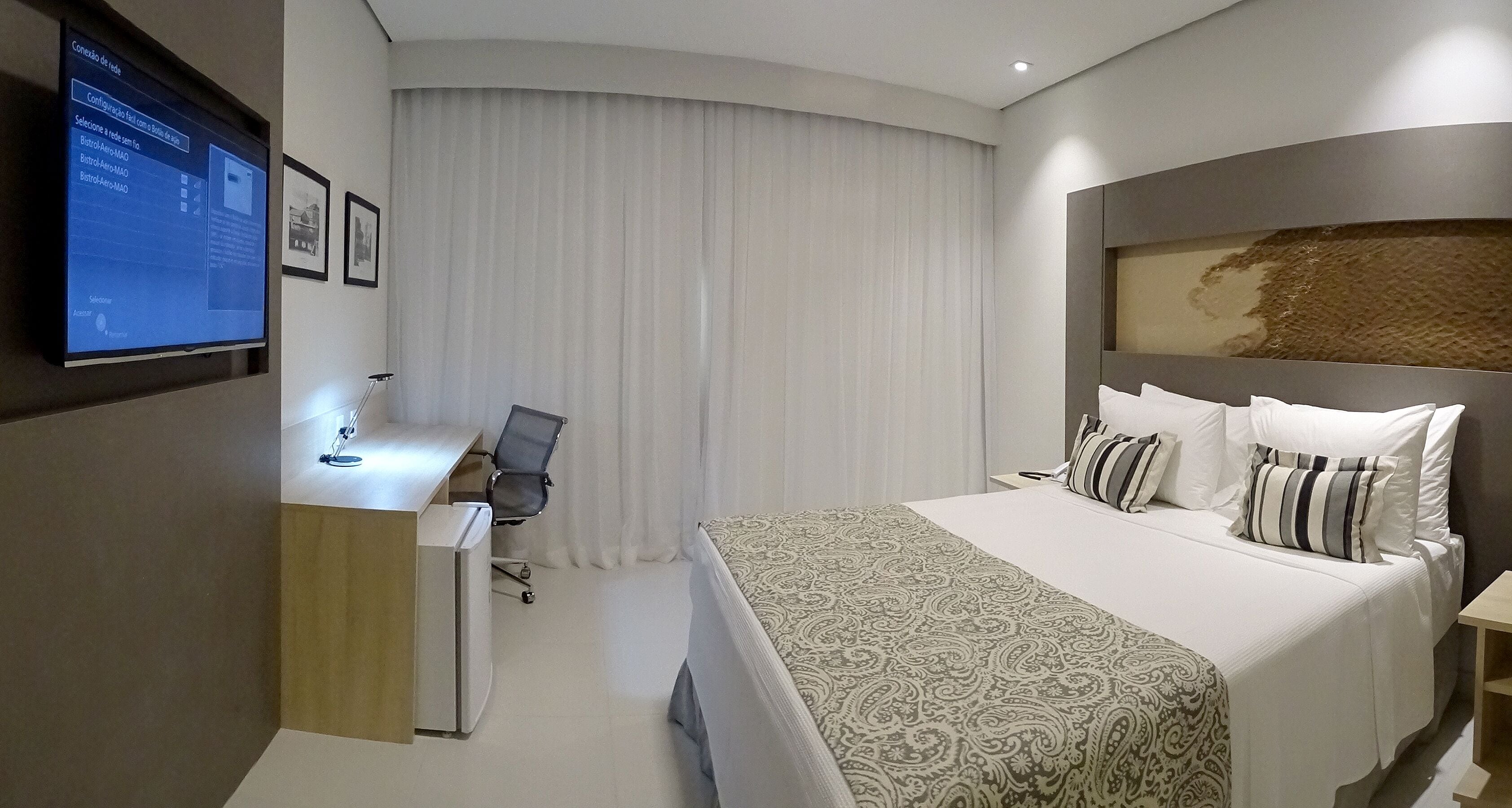 Une chambre d’hôtel équipée d’un lit, d’un bureau, d’une chaise et d’un téléviseur qui affiche un menu.