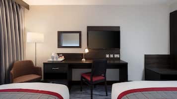 A hotel room with two beds, a desk with a chair, a TV, and a lamp.