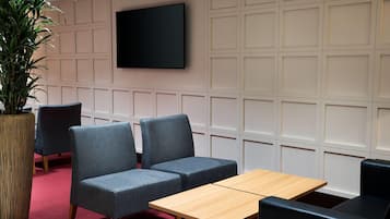 A conference room with a large table, two blue chairs, a potted plant, and a TV mounted on the wall.