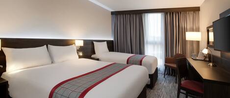 A hotel room with two beds, a desk, a chair, a TV, and a window with curtains.