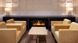 A room with a fireplace, two armchairs, a table, and two lamps. - Ramada by Wyndham Leeds East (Leeds)