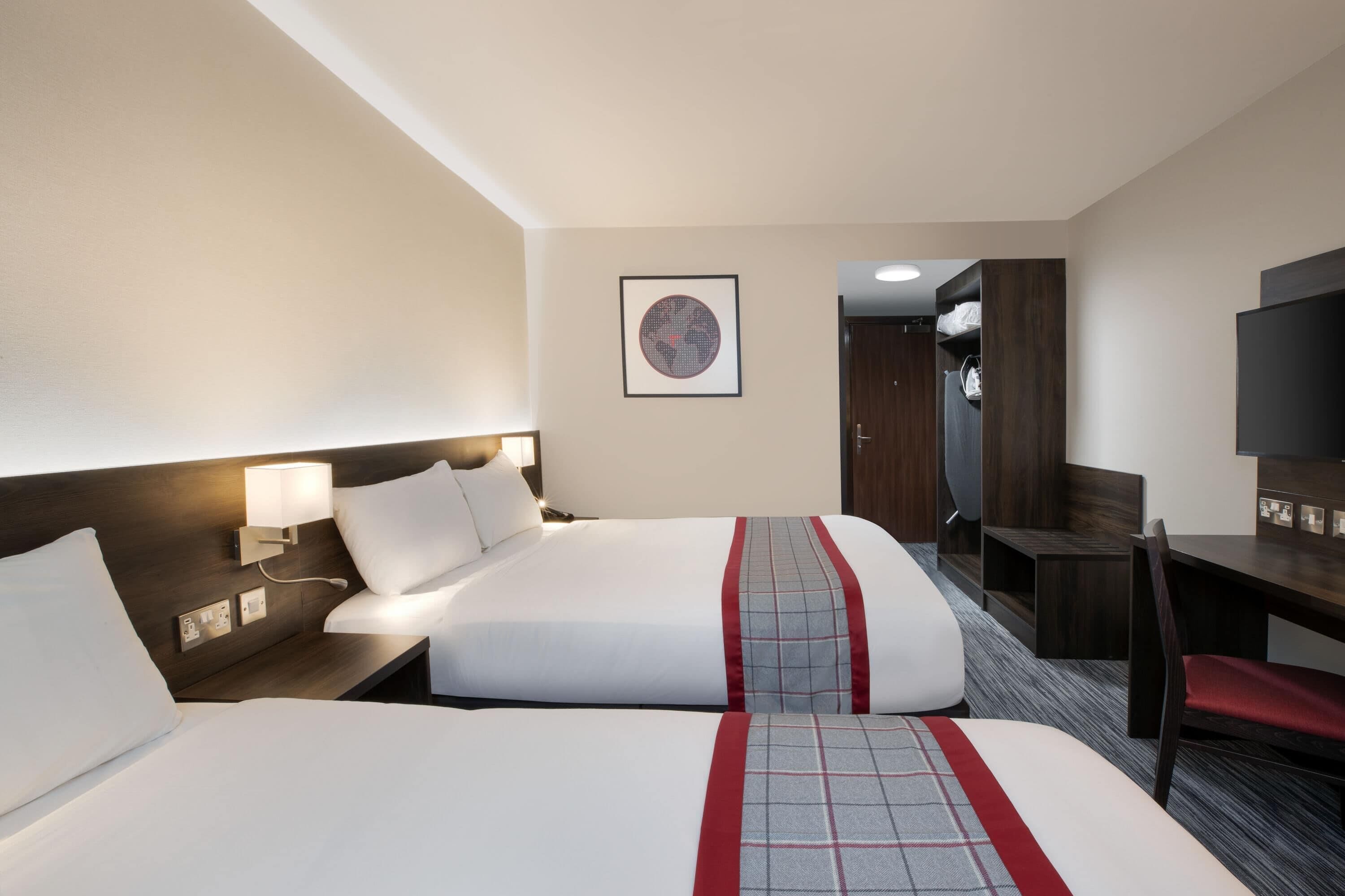Ein Hotelzimmer mit zwei Betten, einem Schreibtisch, einem Stuhl und einem Fernseher.