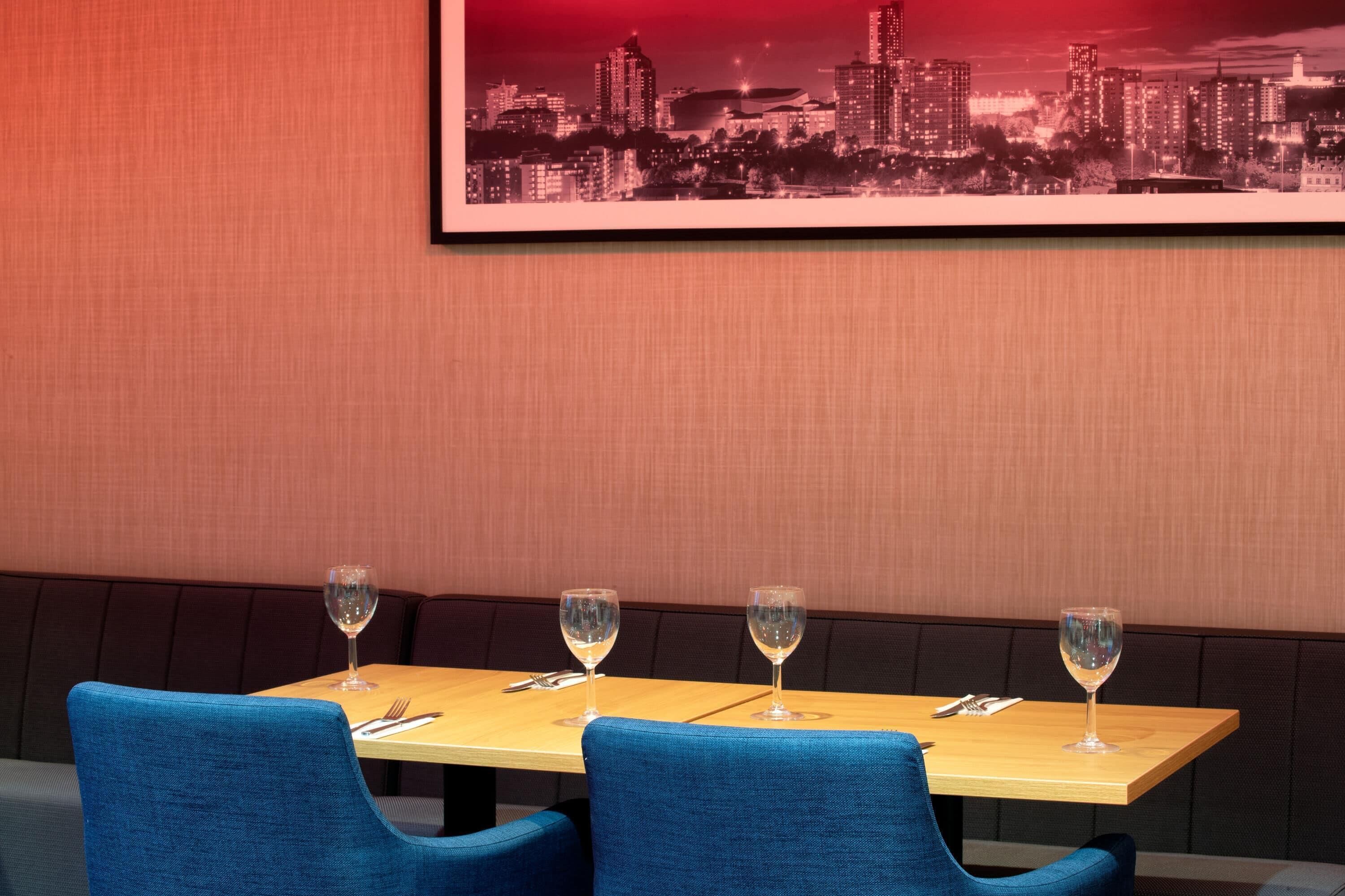 Ein Restaurant mit Blick auf die Stadt, ein Holztisch mit vier Weingläsern und blau gepolsterten Stühlen.