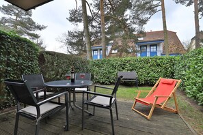 Une terrasse extérieure avec une table ronde, quatre chaises et un fauteuil de jardin rouge.