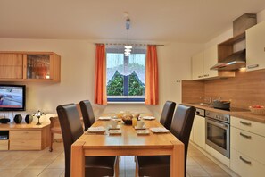Una cocina moderna con comedor, que incluye una mesa de madera, sillas y un televisor sobre un mueble.