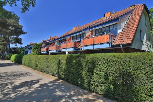 A multi-story hotel with balconies and a well-maintained hedge along the driveway.