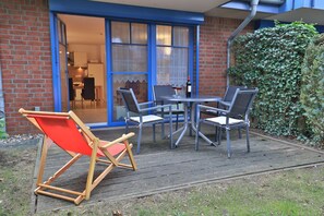 A patio with a table and chairs, a red and wooden chair, and a glass door leading to a room.