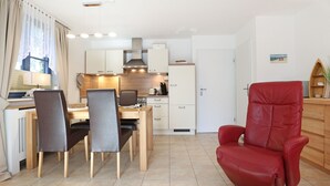 A modern kitchen with white cabinets, a dining area with a table and chairs, and a red leather armchair. - Papillon Whg. 12/4, Germany (Ostseebad Boltenhagen)
