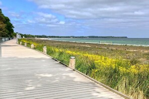 Une promenade en bois qui mène à une plage parsemée de fleurs jaunes et offre une vue sur l’océan.