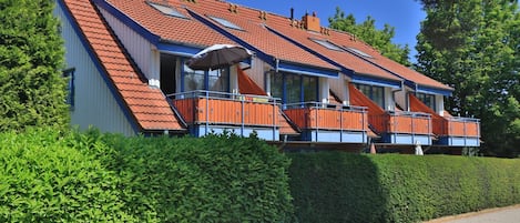 Un bâtiment à deux étages, doté d’un toit en pente, de balcons avec des rampes orange et surplombant un ciel dégagé.