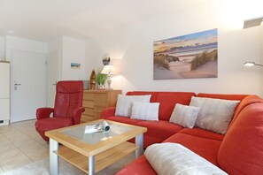 A living room with a red sofa, a glass coffee table, and a painting of a beach scene.