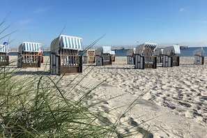 Beach huts with striped awnings, arranged in rows on a sandy beach.