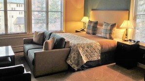 Una habitación de hotel con una cama, dos mesitas de noche, un sofá y una ventana con persianas.
