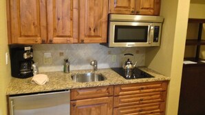 Una cocina con armarios de madera, un microondas de acero inoxidable, una cafetera, un hervidor y un lavavajillas.