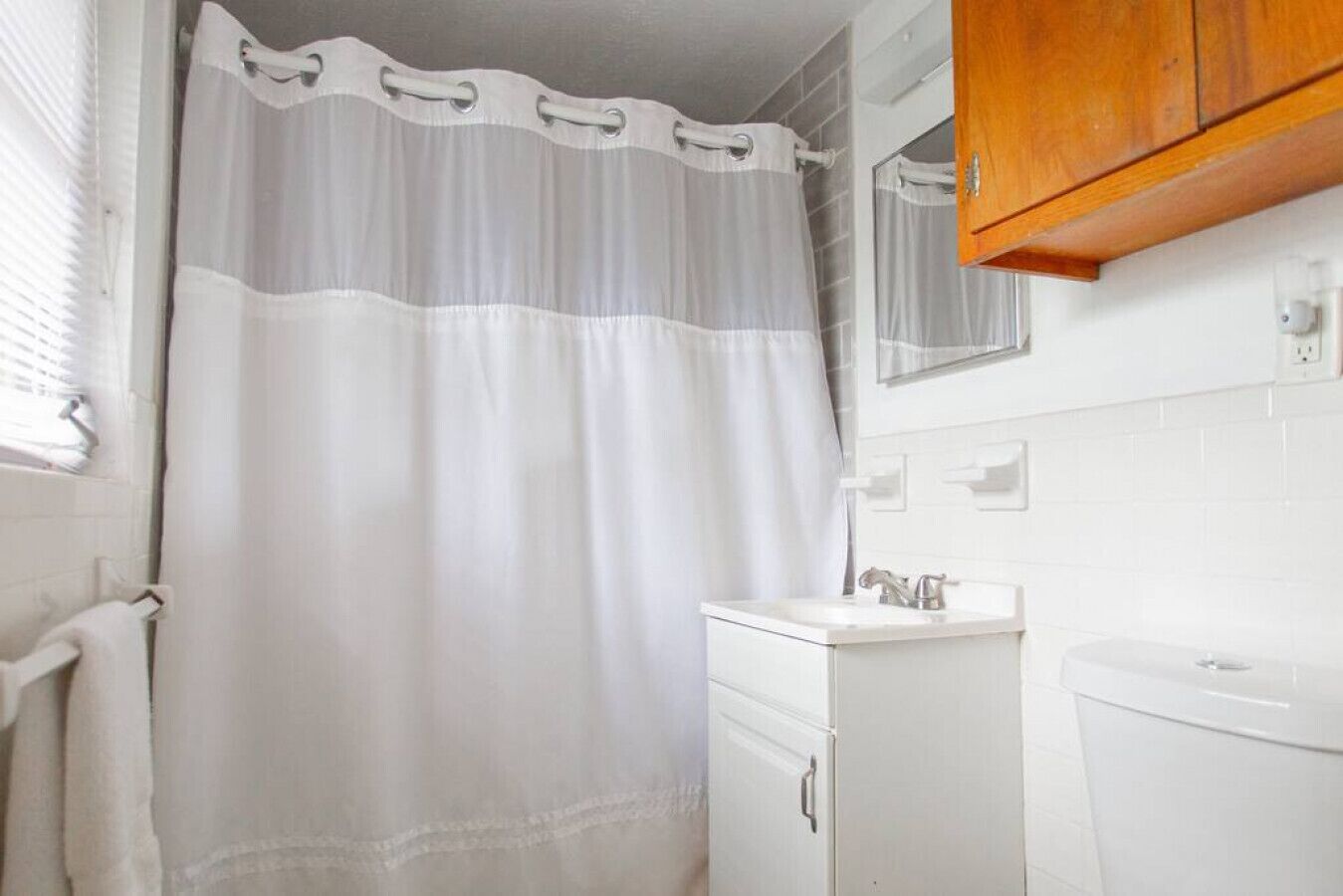 A bathroom with a white shower curtain, a sink, and a wooden cabinet.