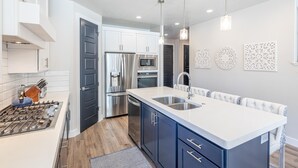 A modern kitchen with white cabinets, stainless steel appliances, and a central island with a sink. - Cliffside Retreat (St. George)
