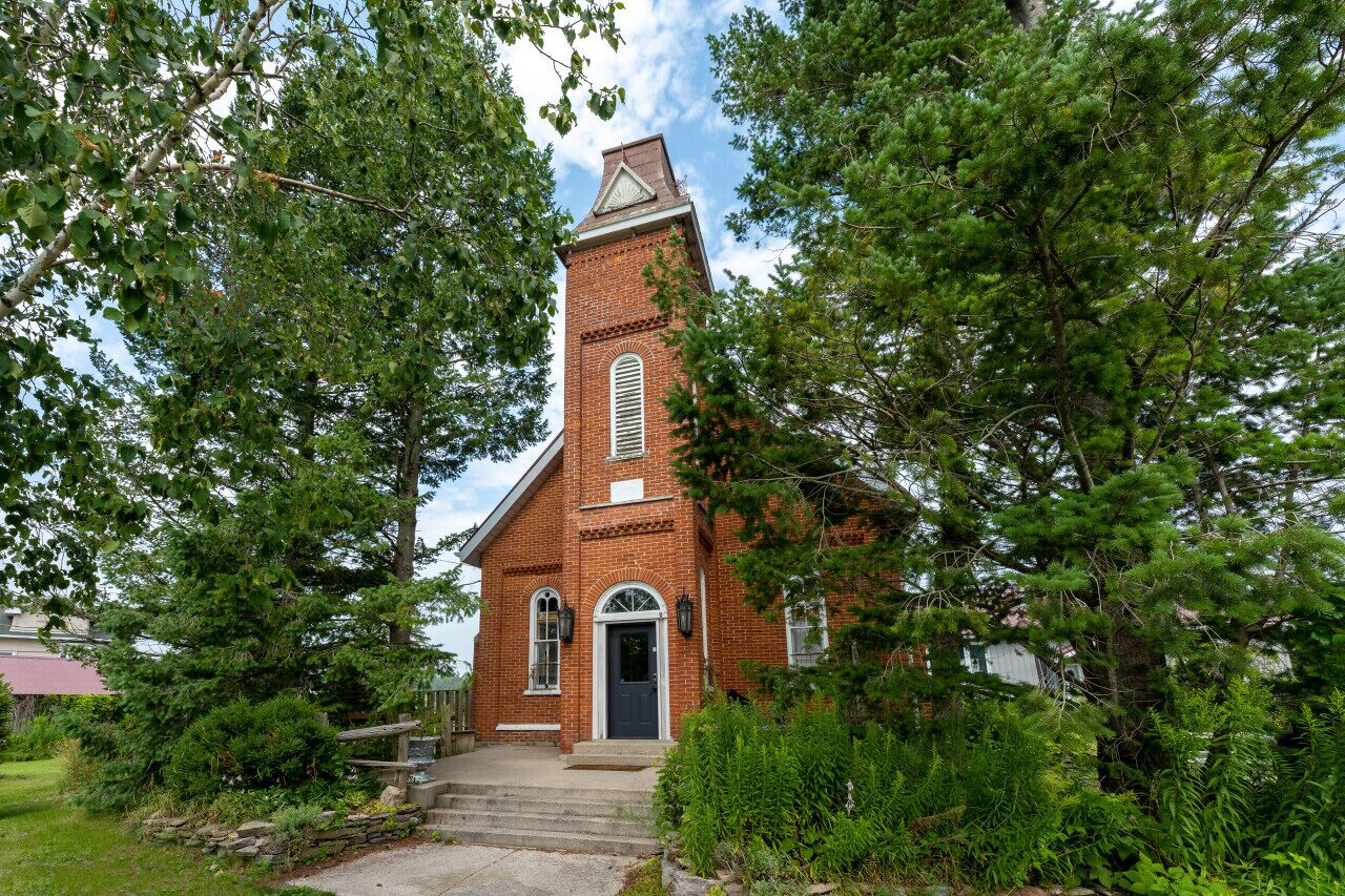 A brick church with a bell tower, surrounded by trees and greenery.