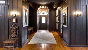 A hallway with dark wooden walls, a wooden floor, and a rug leading to a door with a chandelier.