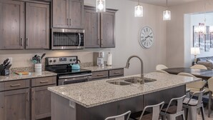 A modern kitchen with granite countertops, stainless steel appliances, and a large island with bar seating. - Poolside Paradise (St. George)