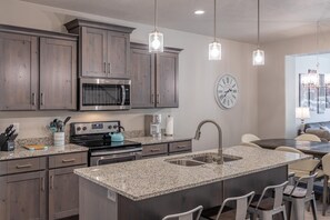 Una cocina moderna con encimeras de granito, electrodomésticos de acero inoxidable y una isla grande con taburetes para bar.