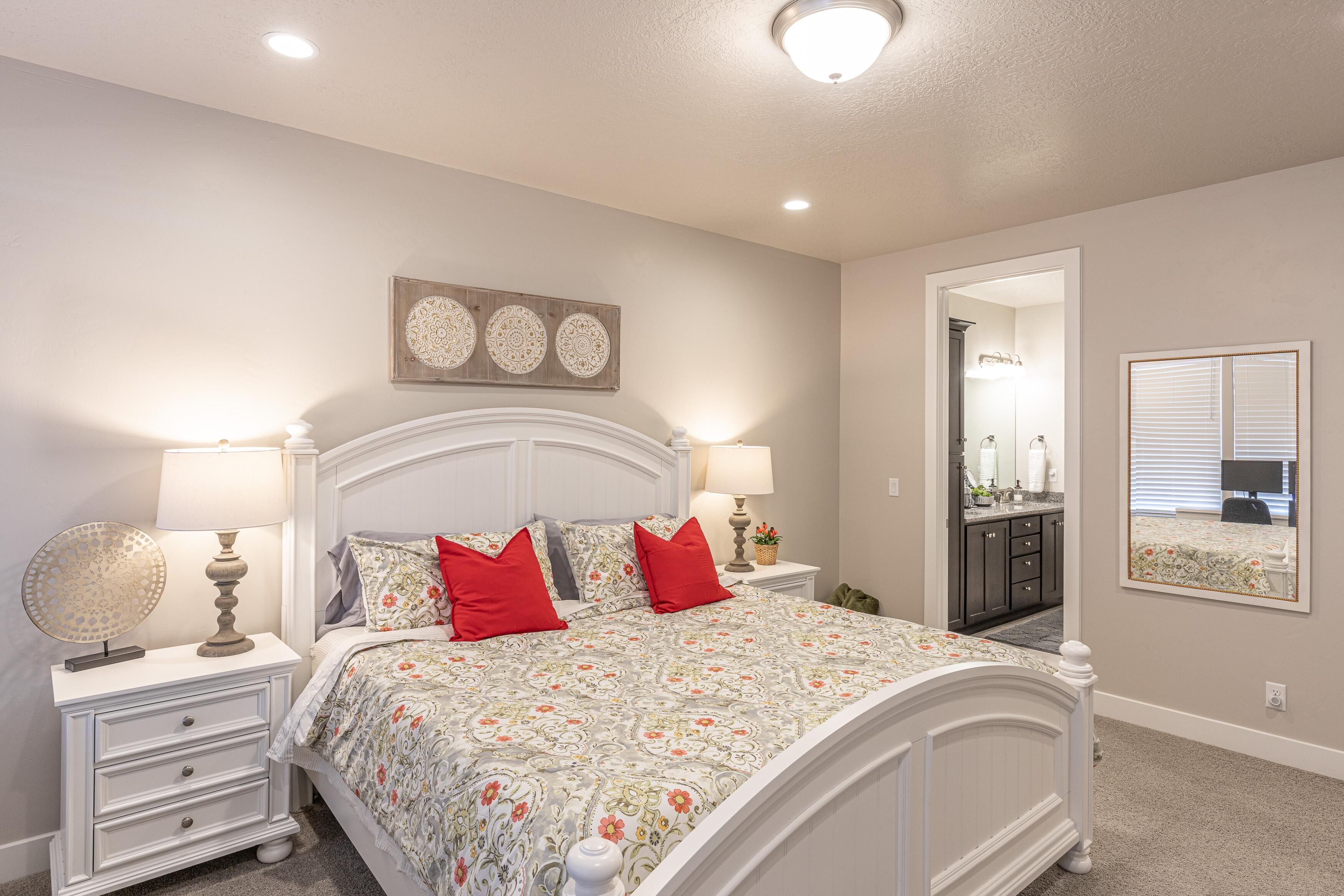 A bedroom with a bed, nightstands, lamps, a mirror, and a wall-mounted artwork.