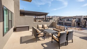 A rooftop patio with outdoor furniture, a pergola, and a view of a cityscape. - Launchpad (St. George)