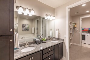 A bathroom with dual sinks, a large mirror, and a walk-in closet with shelves and hanging items. - Launchpad (St. George)