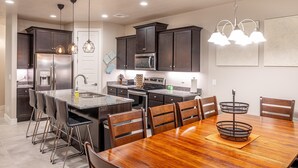 A modern kitchen with dark cabinets, stainless steel appliances, and a wooden dining table. - Launchpad (St. George)