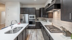 Una cocina moderna con armarios oscuros, electrodomésticos de acero inoxidable, una isla grande con fregadero y una estufa a gas.