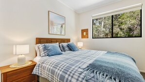 A bedroom with a bed, two bedside lamps, a framed picture, and a window with a view of trees. - Baden 74 - Rainbow Shores. Top Floor - Air conditioned Unit - Walk To Beach (RAINBOW BEACH)