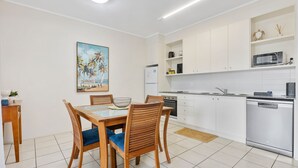 A modern kitchen with white cabinets, a dining table with chairs, a refrigerator, a microwave, and a dishwasher. - Baden 74 - Rainbow Shores. Top Floor - Air conditioned Unit - Walk To Beach (RAINBOW BEACH)